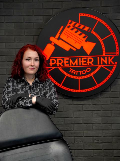 A tetoválóművész a világító Premier Ink logó előtt