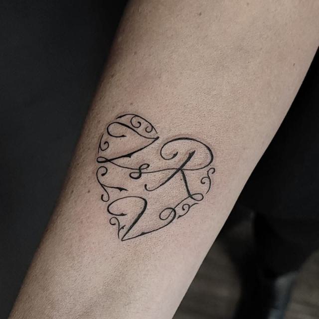 Fineline vonalas tetoválás – szív alakú monogram az alkaron